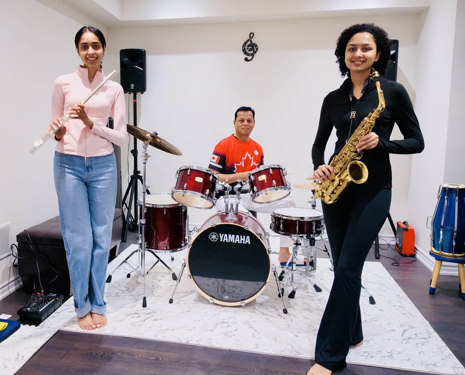 Pankhudi holding a flute on the left, Arvind Choudhary at his drum kit in the centre, and Prachi holding a saxophone on the right, in the family music room.